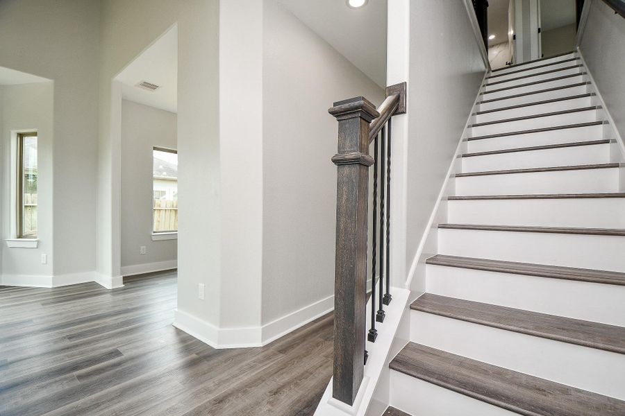 This is a modern interior space featuring a staircase with dark wood accents and metal balusters, complemented by light gray walls and laminate wood flooring. The area is well-lit with natural light from windows and recessed ceiling lights. This is a modern interior space featuring a staircase with dark wood accents and metal balusters, complemented by light gray walls and laminate wood flooring. The area is well-lit with natural light from windows and recessed ceiling lights.