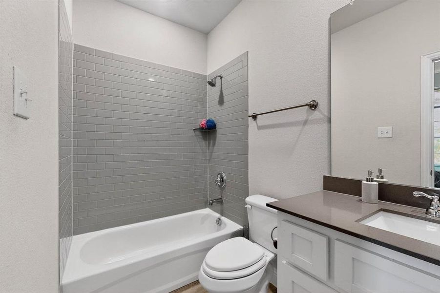 Bathroom featuring shower / tub combination, vanity, and a textured wall Bathroom featuring shower / tub combination, vanity, and a textured wall