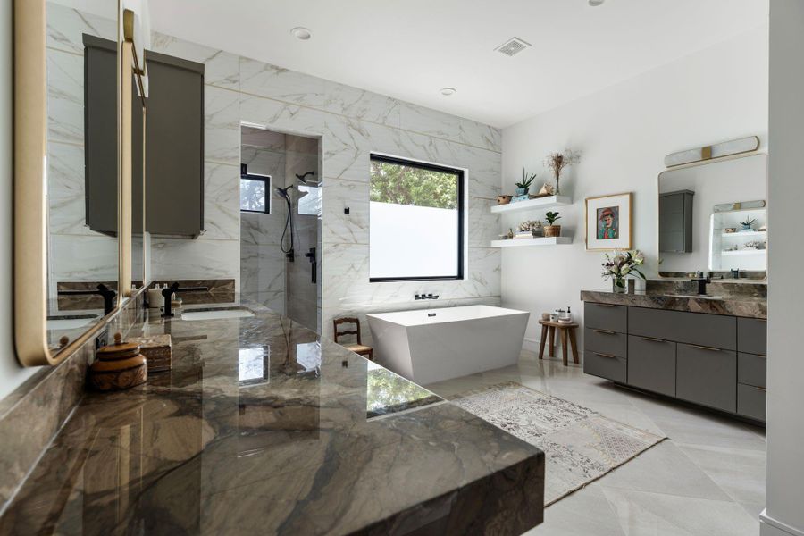 The spa-like primary bath features floating style dual vanities with stone countertops, gold framed mirrors with decorative vanity lighting, and warm gold accents throughout.