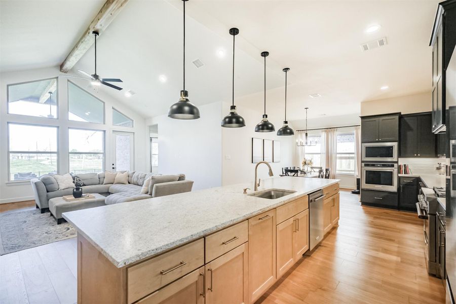 Wide-open great room and kitchen featuring dark cabinetry, massive island with seating, and vaulted ceilings.