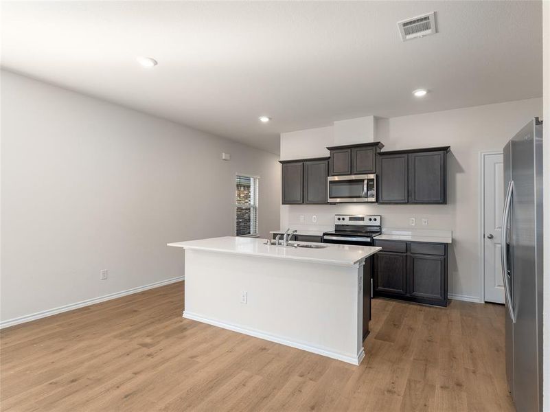 Kitchen with stainless steel appliances, sink, a kitchen island with sink, and light hardwood / wood-style flooring