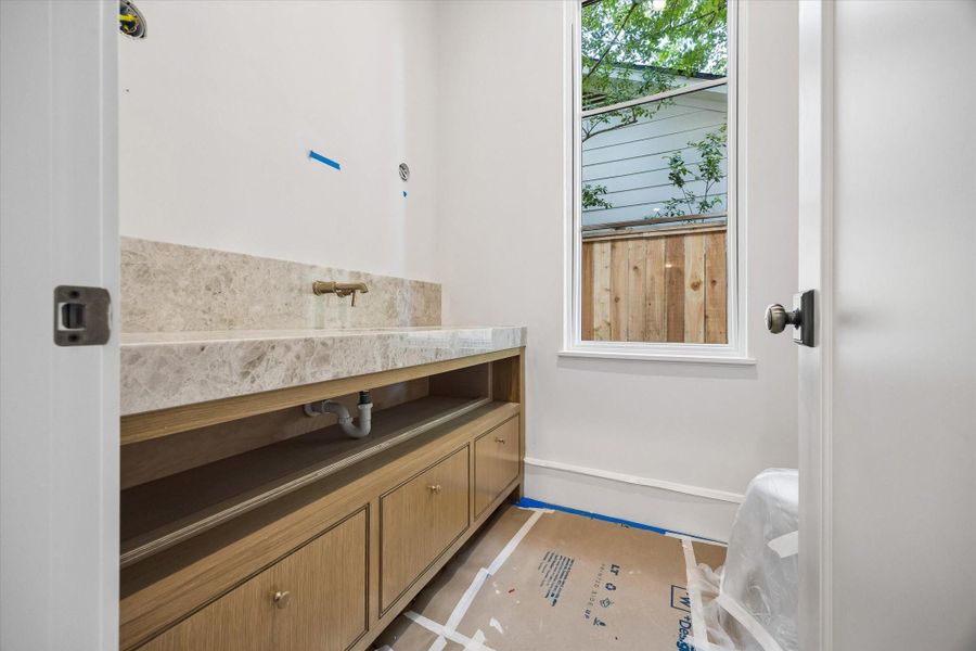 The powder room dazzles with a white oak vanity, brass plumbing fixtures by Brizo, a decorative mirror, and two sconces from Visual Comfort to be installed. The plumbing access will be concealed with a white oak panel for a seamless finish.