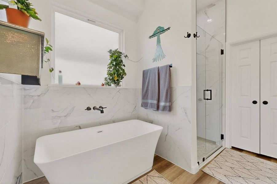 Freestanding soaking tub with a wall-mounted matte black faucet, set against marble-look tile wainscoting