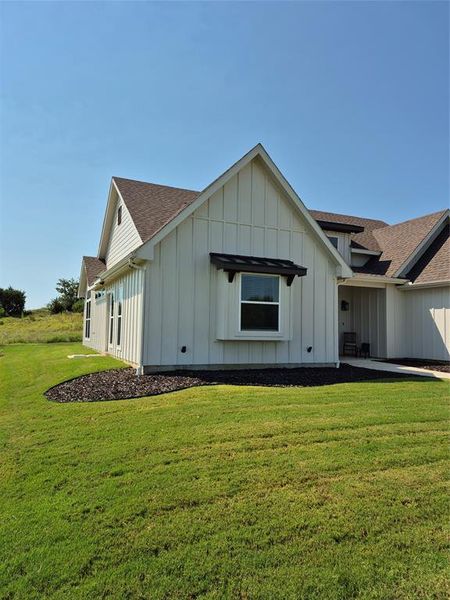 View of side of property with board and batten siding, roof with shingles, and a yard