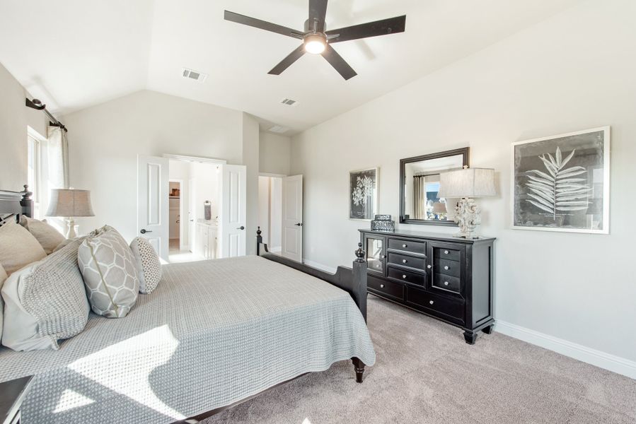 Master bedroom with vaulted ceiling, ceiling fan, dark wood dresser, and carpet flooring with ensuite bathroom access Master bedroom with vaulted ceiling, ceiling fan, dark wood dresser, and carpet flooring with ensuite bathroom access