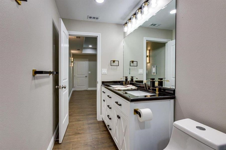 Half bath featuring a textured wall, dark wood finished floors, double vanity, and recessed lighting