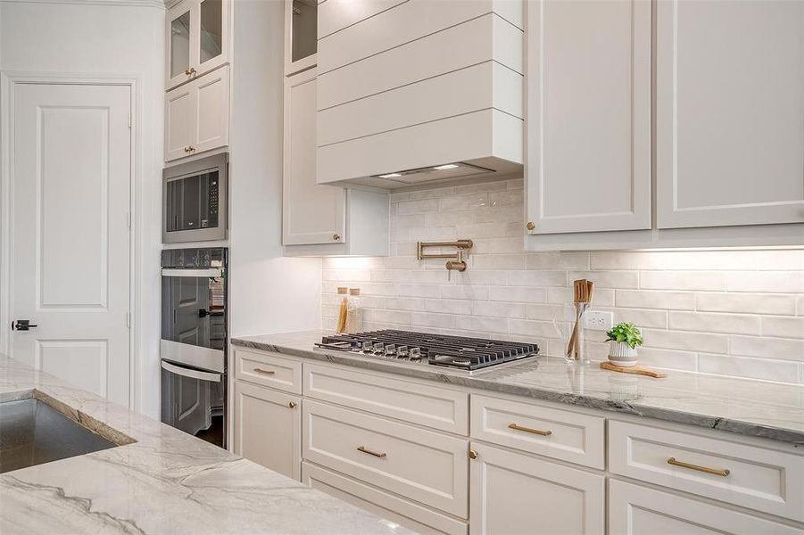 Kitchen featuring a large island, gold hardware, decorative light fixtures, custom cabinetry to the ceiling, gas cooktop, double oven and walk in pantry