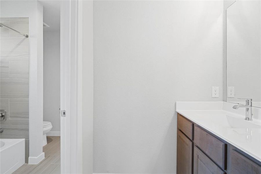 Secondary bath features a private vanity area and then opens to a shared tub/shower combo and toilet. Features include tile flooring, bath/shower combo with tile surround, wood stained cabinets, beautiful light countertops, mirror, dark, sleek fixtures and modern finishes!