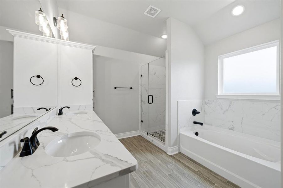 Full bathroom with double vanity, a marble finish shower, a bath, wood finish floors, and vaulted ceiling