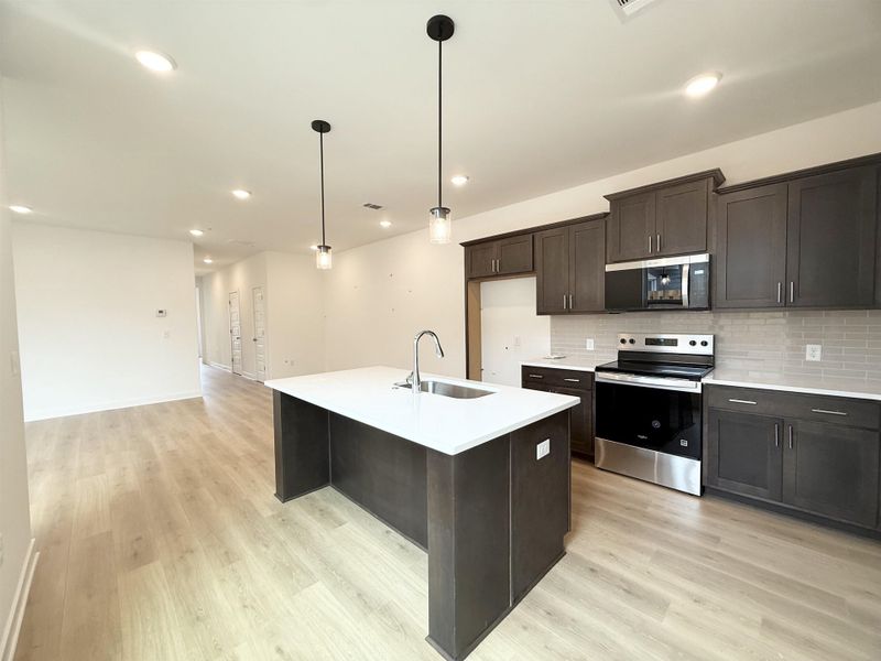 Kitchen featuring stainless steel appliances, a sink, light wood-type flooring, backsplash, and light countertops Kitchen featuring stainless steel appliances, a sink, light wood-type flooring, backsplash, and light countertops