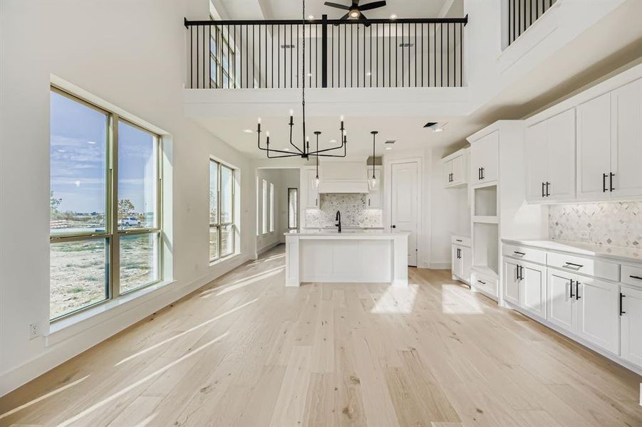 Kitchen with decorative light fixtures, decorative backsplash, white cabinets, light wood-style flooring, and an island with sink Kitchen with decorative light fixtures, decorative backsplash, white cabinets, light wood-style flooring, and an island with sink