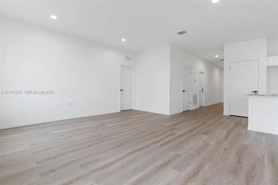 Wood-finish flooring, recessed lighting, white interior doors with matte black hardware, and a stone-surface breakfast bar Wood-finish flooring, recessed lighting, white interior doors with matte black hardware, and a stone-surface breakfast bar