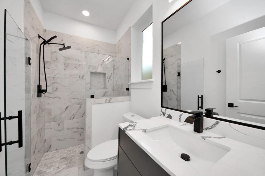 This photo showcases a modern bathroom with a sleek design. It features a spacious glass-enclosed shower with a rainfall showerhead, elegant marble tile, a stylish vanity with a large mirror, and contemporary black fixtures. This photo showcases a modern bathroom with a sleek design. It features a spacious glass-enclosed shower with a rainfall showerhead, elegant marble tile, a stylish vanity with a large mirror, and contemporary black fixtures.