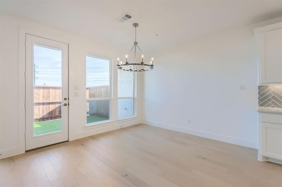 Unfurnished dining area with light wood-type flooring, a healthy amount of sunlight, and a notable chandelier