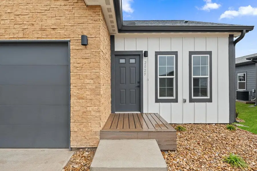 Entrance to property with board and batten siding, stone siding, a garage, and roof with shingles