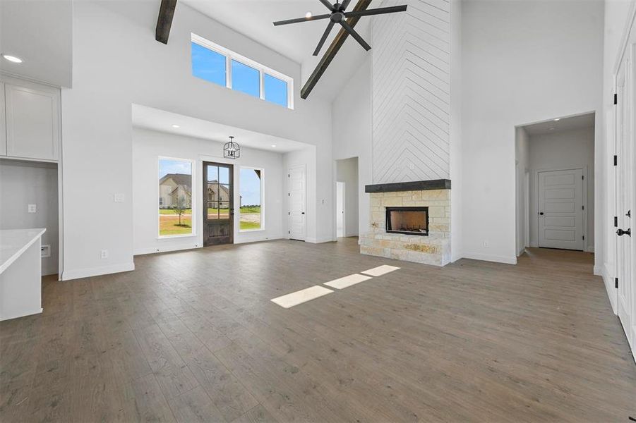 Unfurnished living room featuring high vaulted ceiling, ceiling fan, a stone fireplace, and dark wood-type flooring