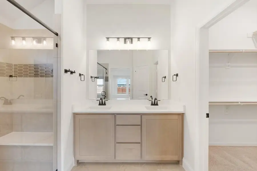 Master bathroom with double vanity, glass shower, tile surround, and walk-in closet entrance