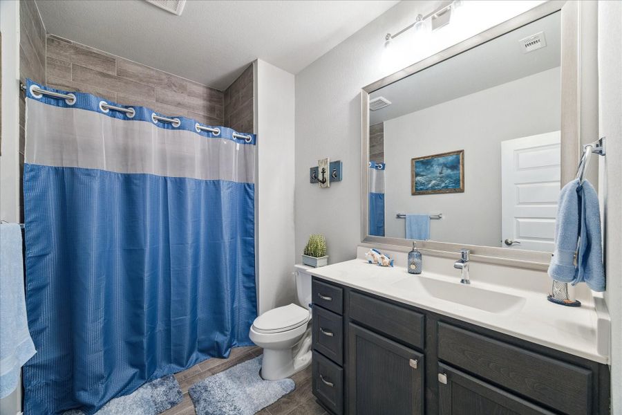 Bright bathroom with a walk-in shower, blue accents, and a large mirror above a dark vanity. Bright bathroom with a walk-in shower, blue accents, and a large mirror above a dark vanity.