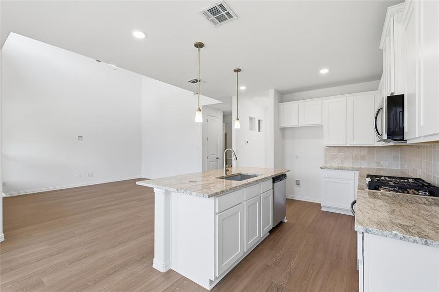 Kitchen with white cabinetry, a kitchen island with sink, decorative light fixtures, backsplash, and dark wood finished floors