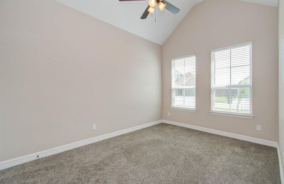 This is a spacious and well-lit room featuring neutral walls, carpeted flooring, and two windows providing ample natural light, complete with a ceiling fan for comfort.