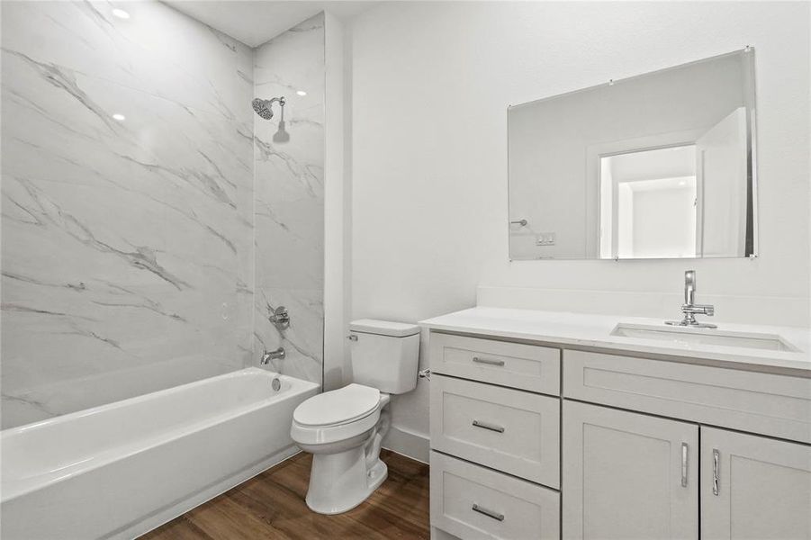 Full bathroom featuring a combined bath / shower with marble appearance, dark wood-type flooring, and vanity