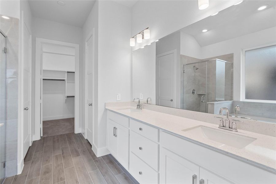 This stunningly updated primary bathroom is truly move-in ready! It features white cabinetry with light countertops, dual vanities, a large mirror, a generous walk-in closet with built-in shelving, soaring ceilings, custom paint, and sleek modern fixtures.