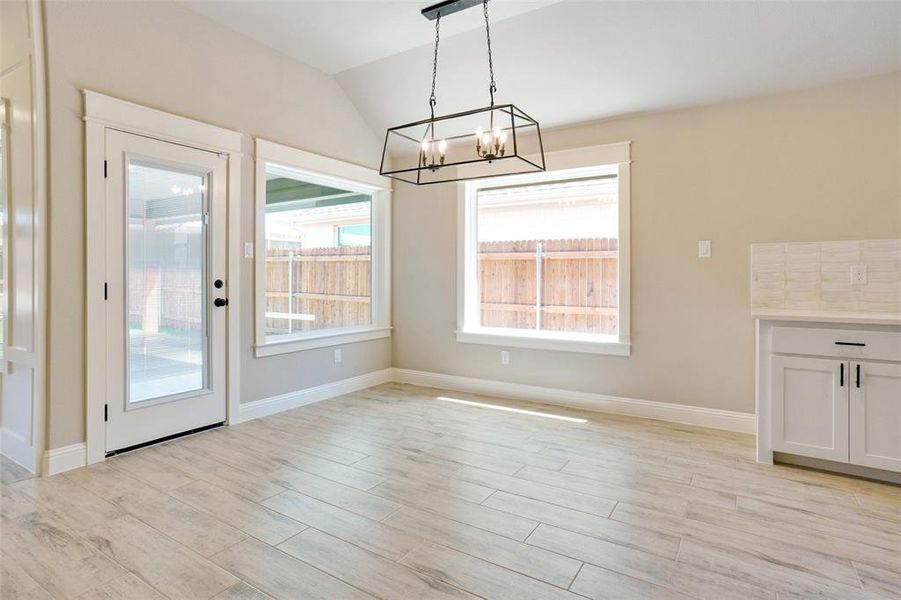 Unfurnished dining area with an inviting chandelier, light wood-type flooring, and vaulted ceiling