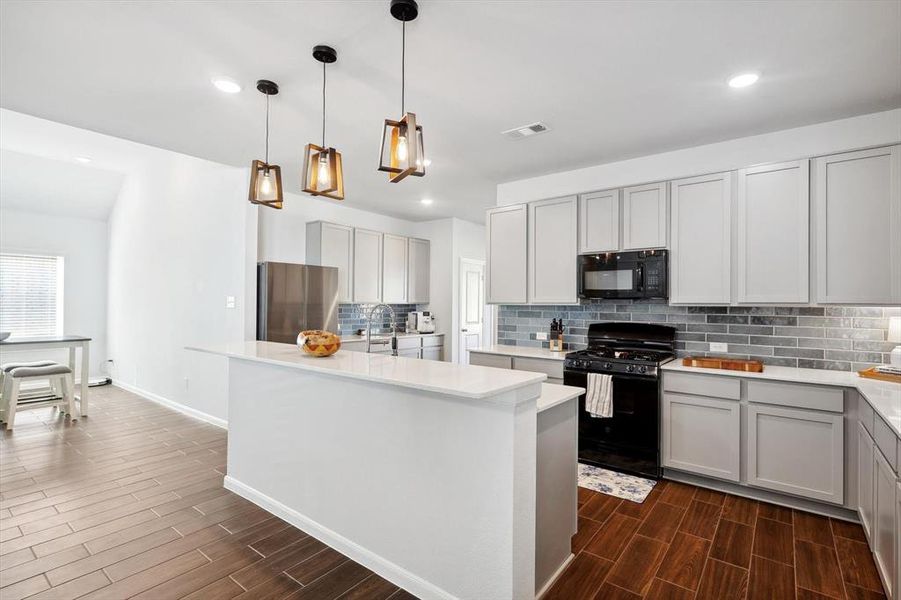 Kitchen with dark hardwood / wood-style flooring, gray cabinetry, black appliances, and an island with sink