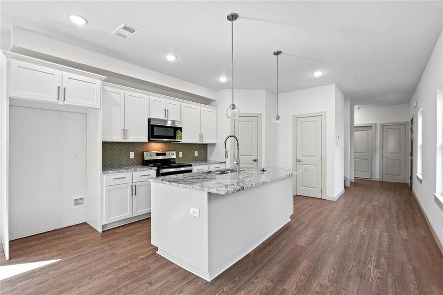 Kitchen featuring appliances with stainless steel finishes, white cabinetry, light stone countertops, decorative backsplash, and a center island with sink