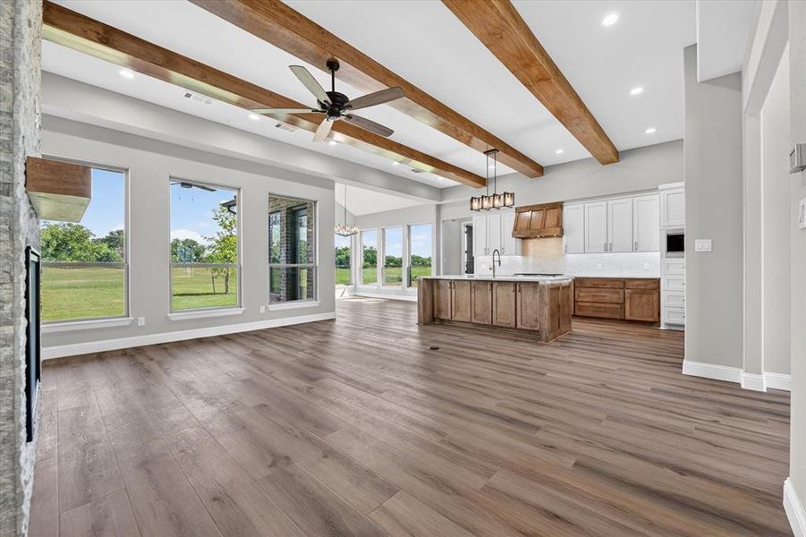 Open-concept living area featuring wood-finish flooring, a stone fireplace, and exposed wood ceiling beams