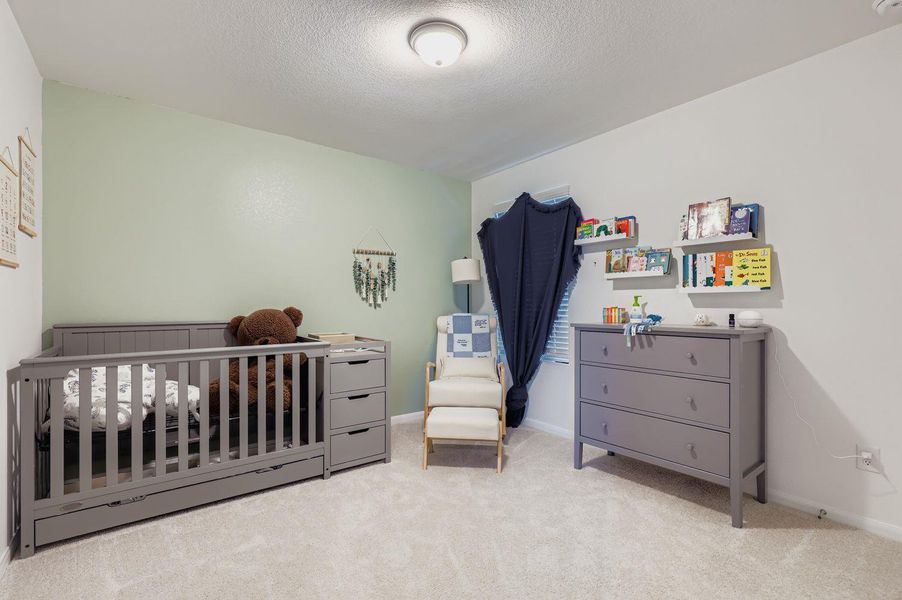 Bedroom with a nursery area, light colored carpet, and a textured ceiling