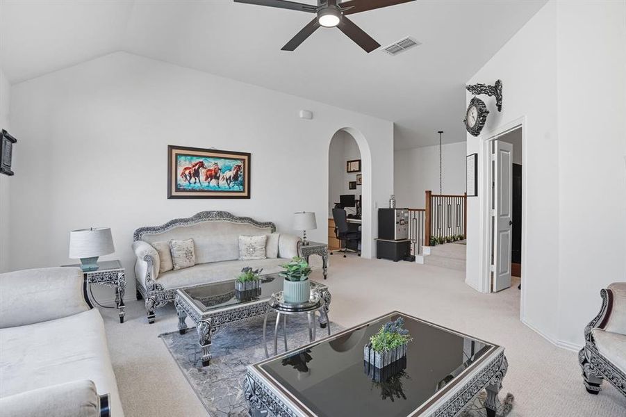 Living area with vaulted ceiling, light carpet, a ceiling fan, arched walkways, and an office area