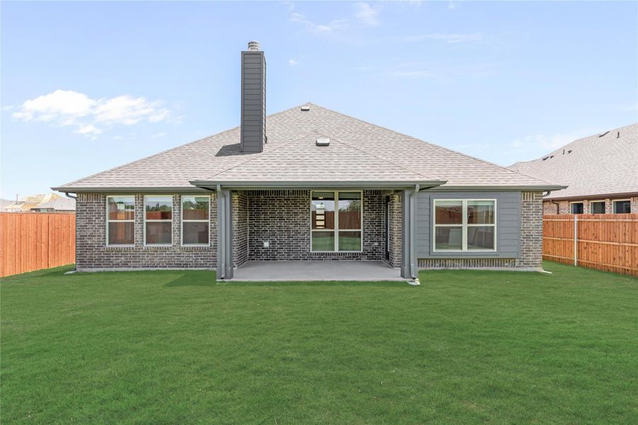 Rear exterior of brick home with covered patio, chimney, and fenced backyard with green lawn
