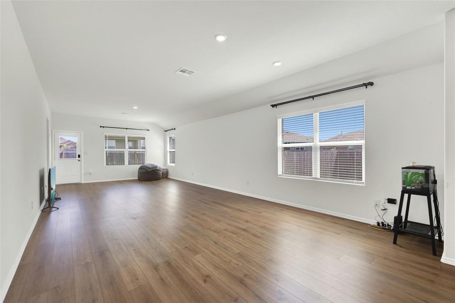 Rich hardwood floors extend through this open-concept living area, bathed in natural light from multiple windows.