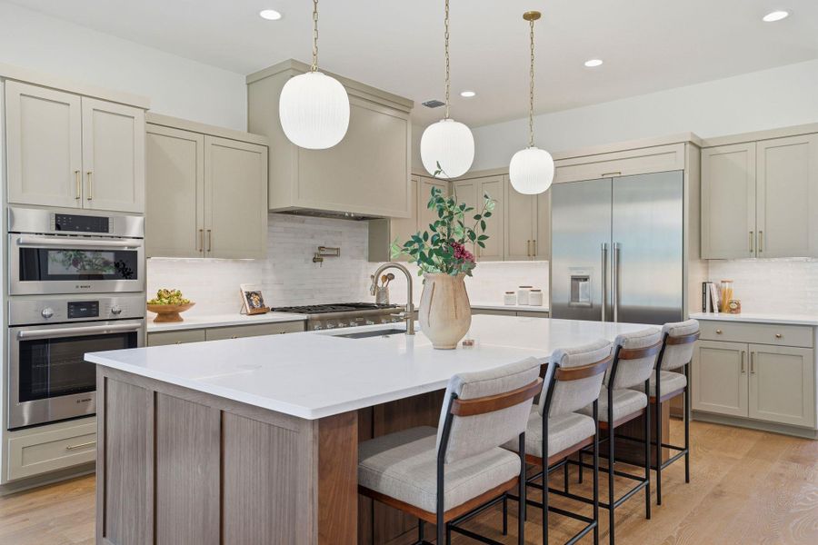 Kitchen with stainless steel appliances, decorative light fixtures, backsplash, a center island with sink, and light wood-type flooring