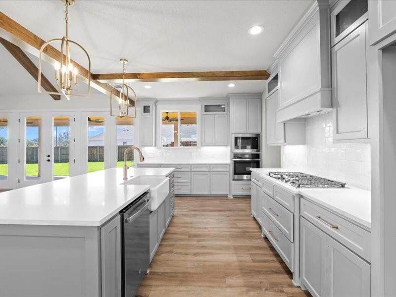 Kitchen featuring glass insert cabinets, hanging light fixtures, stainless steel appliances, beam ceiling, and light wood finished floors Kitchen featuring glass insert cabinets, hanging light fixtures, stainless steel appliances, beam ceiling, and light wood finished floors