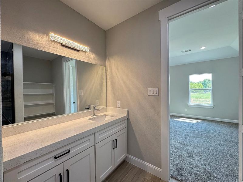 Bathroom vanity featuring a vessel sink, a light-toned countertop, and white cabinetry with matte black hardware