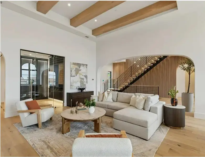 Living area featuring stairs, arched walkways, a towering ceiling, light wood-style flooring, and beamed ceiling