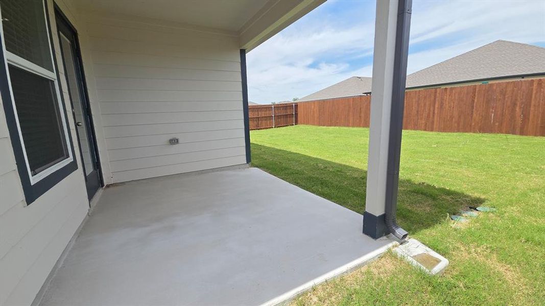 Covered concrete patio opening to a spacious grassy yard