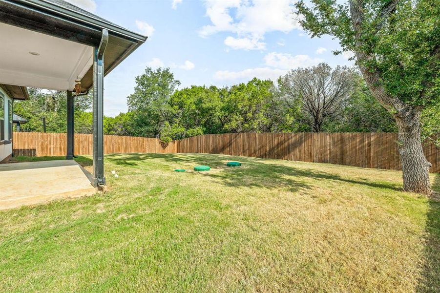 Fenced backyard with a patio and view of scattered trees Fenced backyard with a patio and view of scattered trees