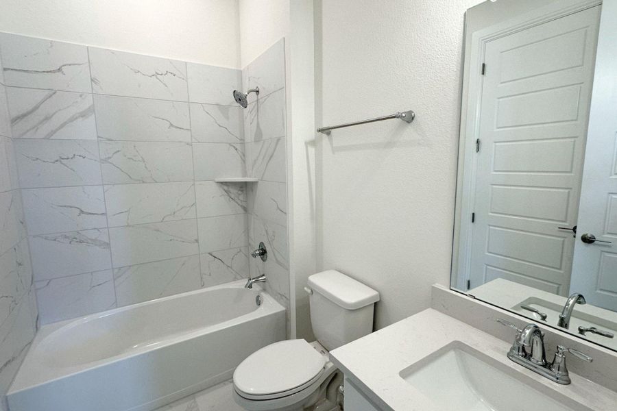 A well-lit primary bathroom features a pristine bathtub and vanity with generous counter space.