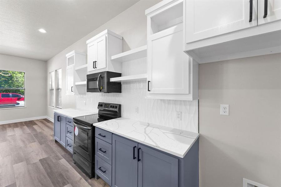 Kitchen with light stone counters, white cabinets, tasteful backsplash, light hardwood / wood-style flooring, and electric range