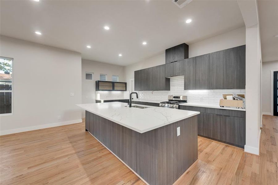 Kitchen featuring stainless steel gas range oven, tasteful backsplash, a kitchen island with sink, light wood-type flooring, and sink