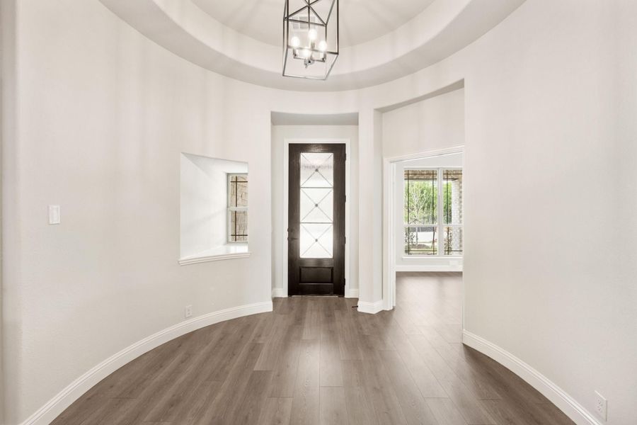 Curved foyer with domed ceiling, dark wood front door, chandelier, and hardwood floors