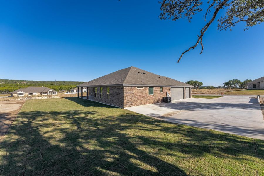 View of side of property featuring a lawn, brick siding, concrete driveway, and roof with shingles