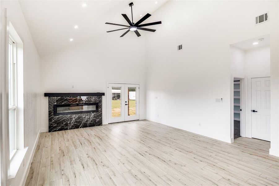Unfurnished living room with a high end fireplace, high vaulted ceiling, light wood-style floors, a ceiling fan, and recessed lighting Unfurnished living room with a high end fireplace, high vaulted ceiling, light wood-style floors, a ceiling fan, and recessed lighting