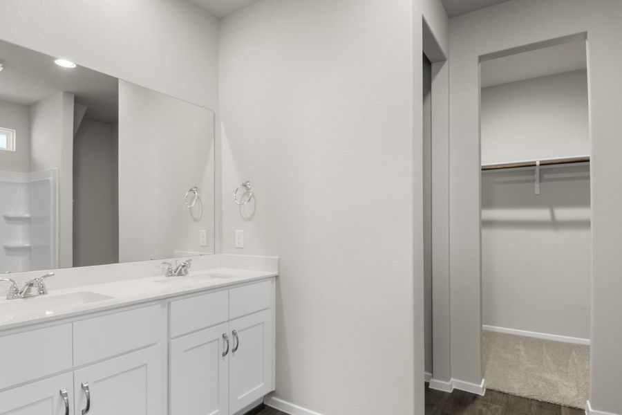 image of a primary bathroom with a double vanity, white cabinets, a large mirror, a semi-private water closet and a walk-in closet