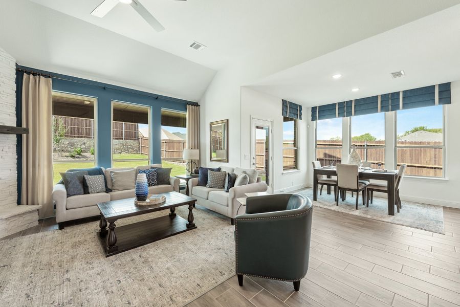 Open living and dining area with vaulted ceiling, large windows, wood-look floors, and blue accent curtains