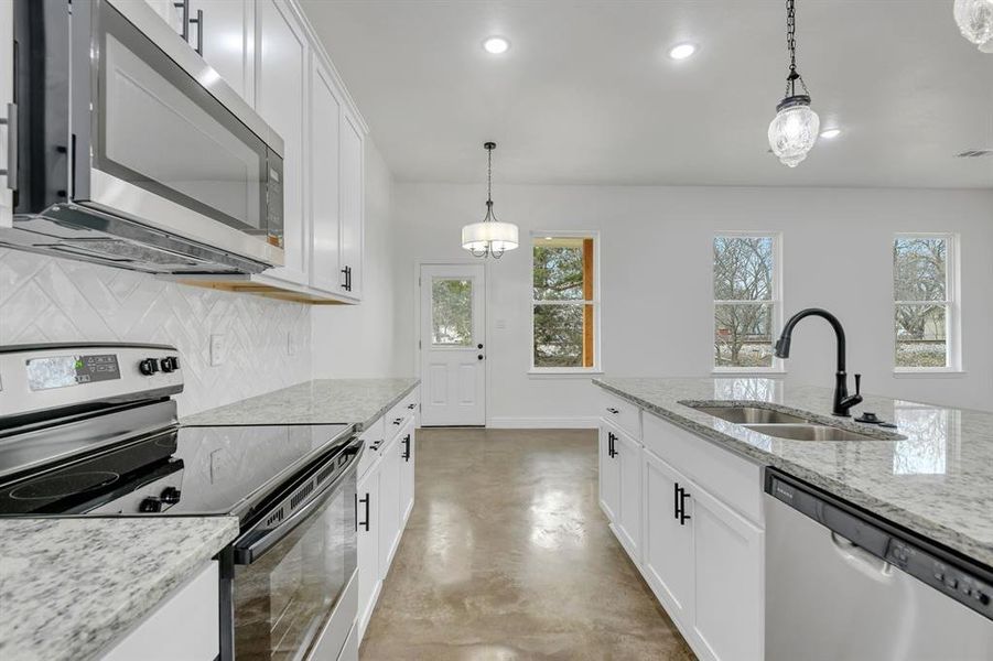 Kitchen featuring appliances with stainless steel finishes, finished concrete floors, white cabinetry, light stone countertops, and hanging light fixtures