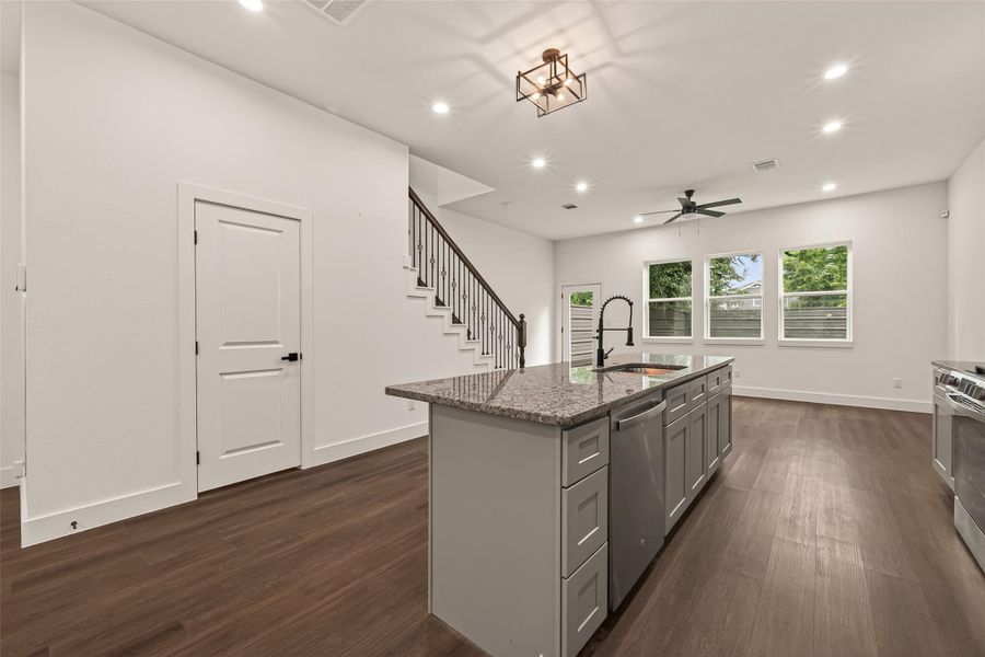 This photo showcases a modern open-plan kitchen and living area featuring sleek engineer wood floors, a large island with granite countertops, stainless steel appliances, and recessed lighting. The space is brightened by ample natural light from multiple windows, and there's a contemporary ceiling fan for added comfort. This photo showcases a modern open-plan kitchen and living area featuring sleek engineer wood floors, a large island with granite countertops, stainless steel appliances, and recessed lighting. The space is brightened by ample natural light from multiple windows, and there's a contemporary ceiling fan for added comfort.